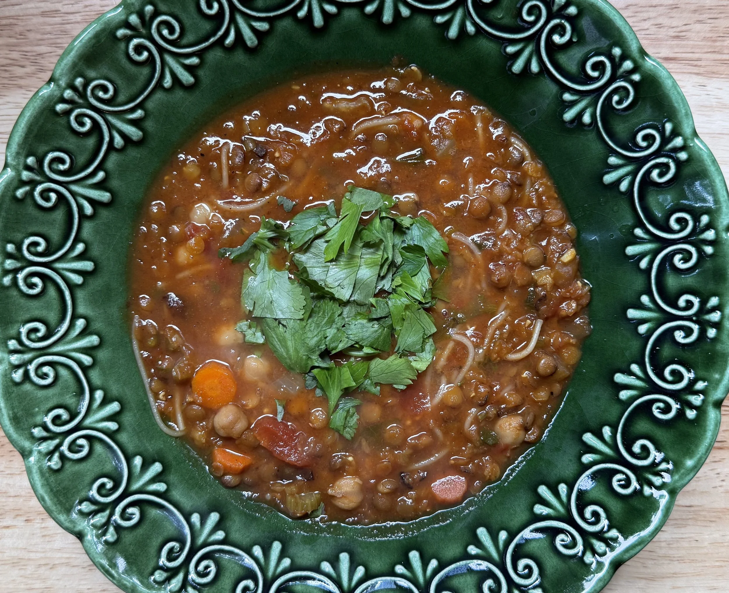 A bowl of lentil soup garnished with fresh cilantro, served in a green decorative bowl on a wooden surface.