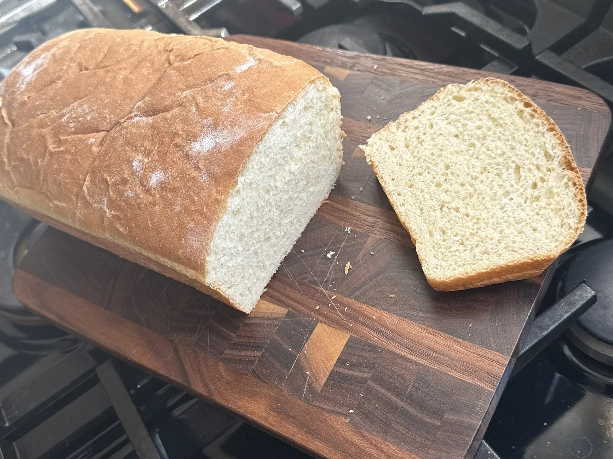 A loaf of white bread with a slice cut from it, placed on a wooden cutting board.