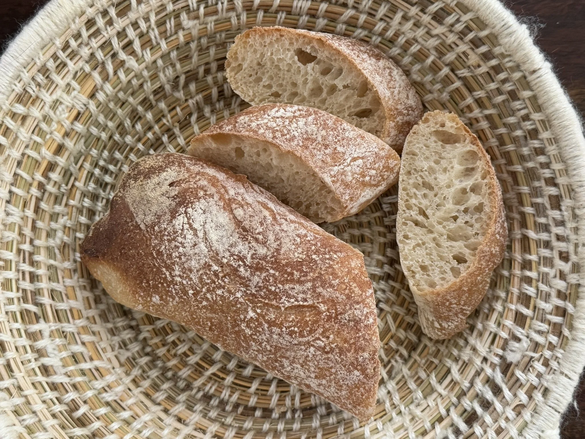 Sliced ciabatta  with a golden crust and a light dusting of flour, placed in a woven basket.