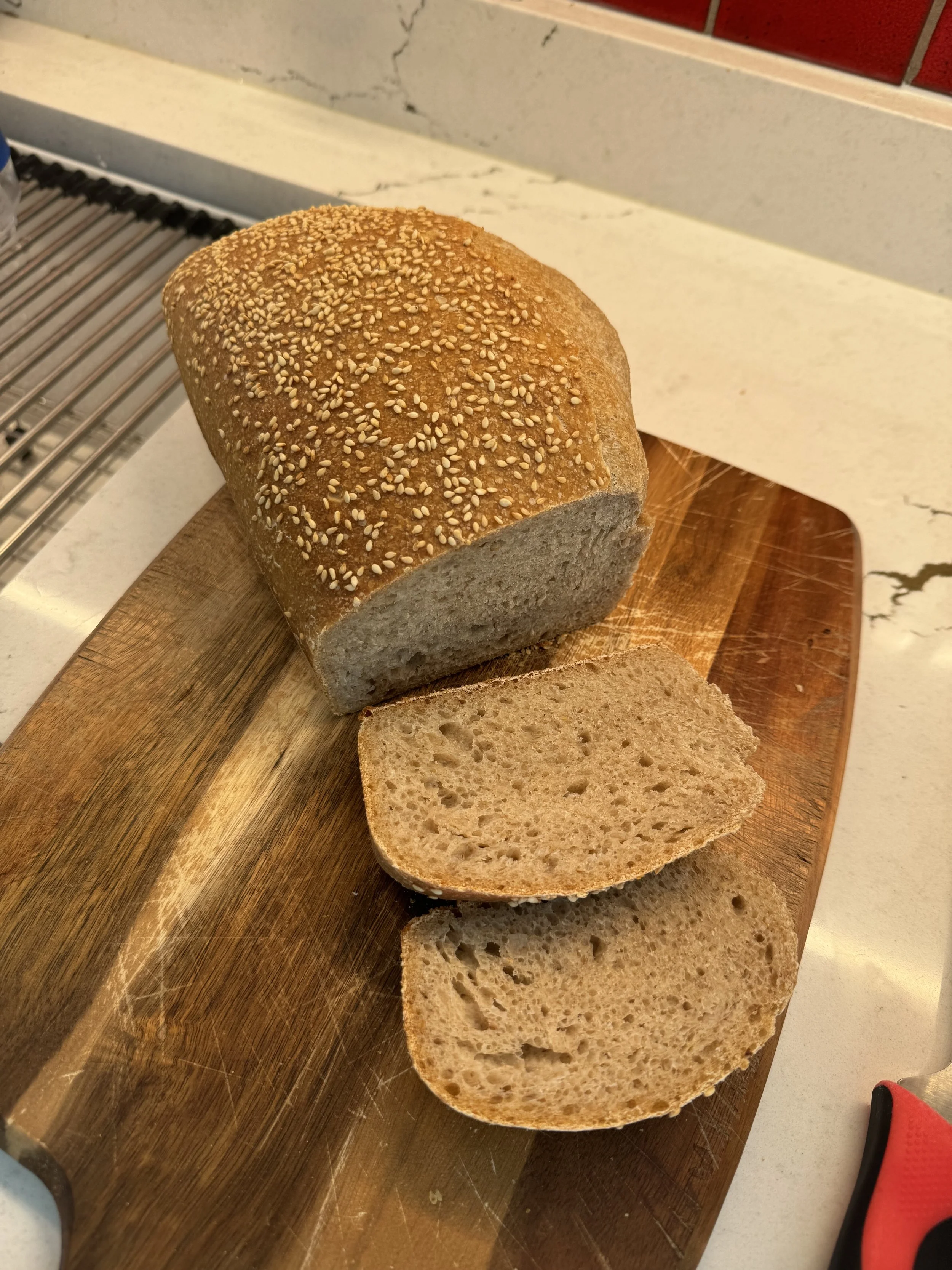 Sliced loaf of bread with sesame seed topping on a wooden cutting board.