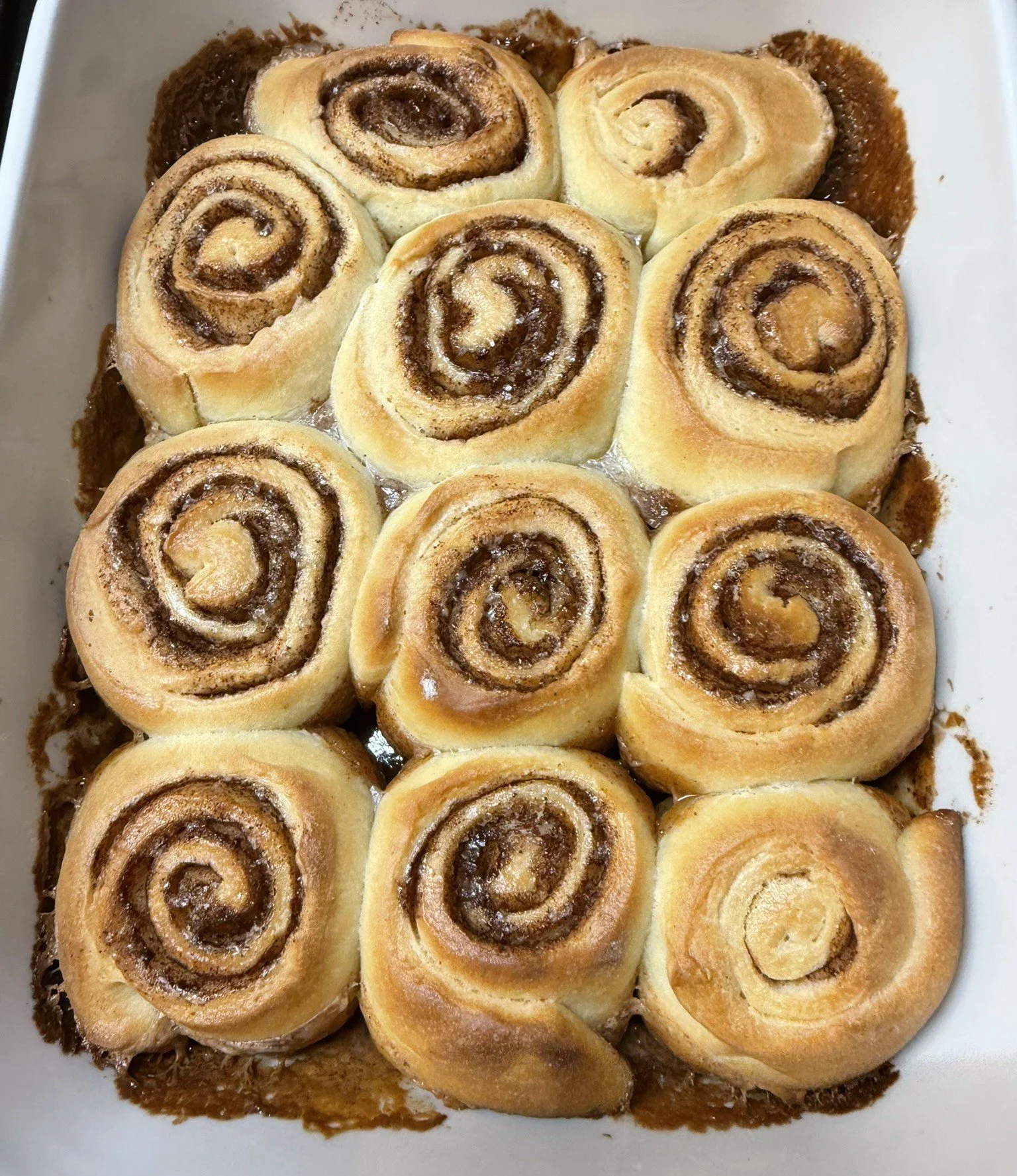 A baking dish filled with cinnamon rolls topped with a drizzle of icing, arranged closely together.
