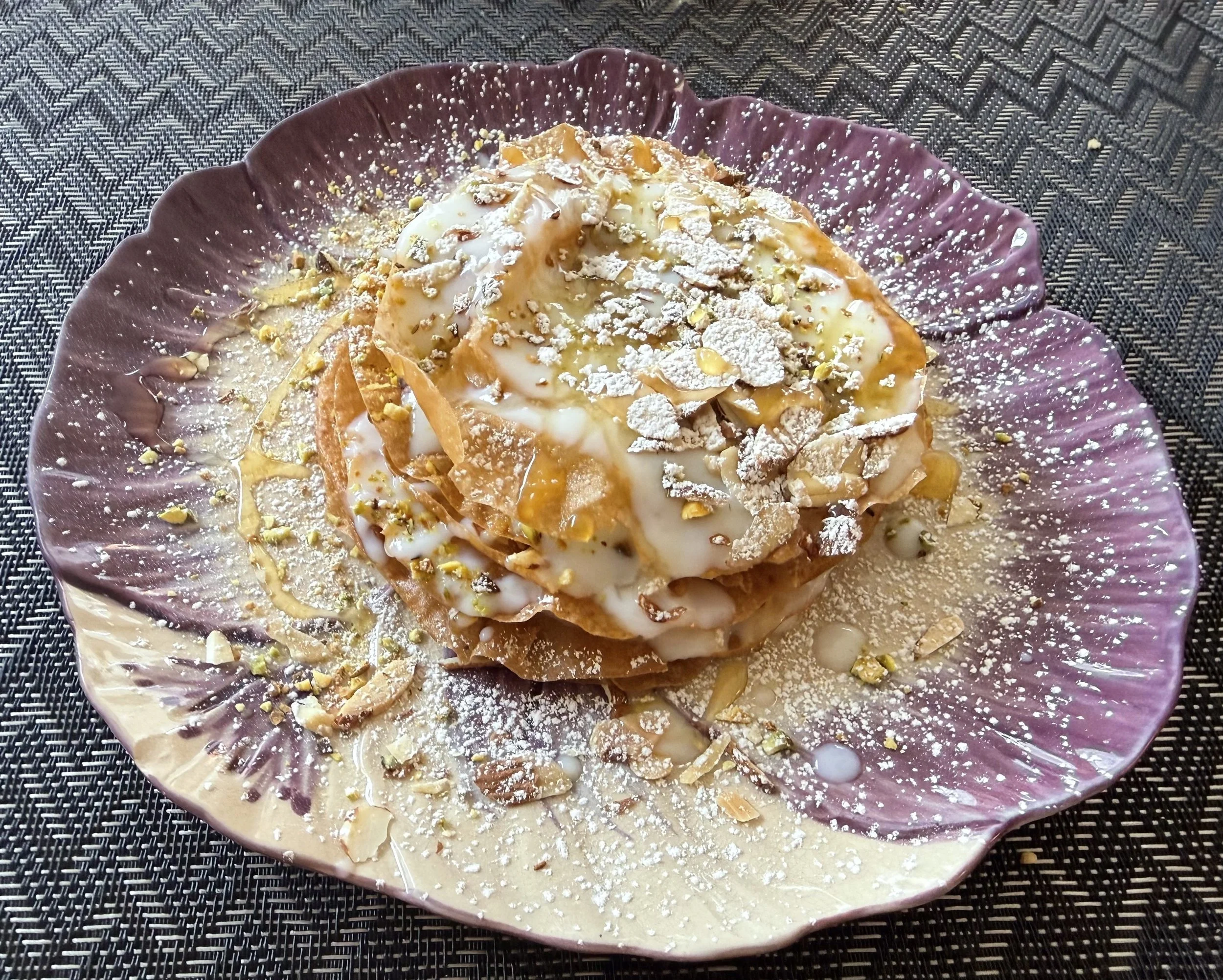 A dessert with cookies and cream ice cream, topped with crushed nuts and powdered sugar on a decorative purple plate.