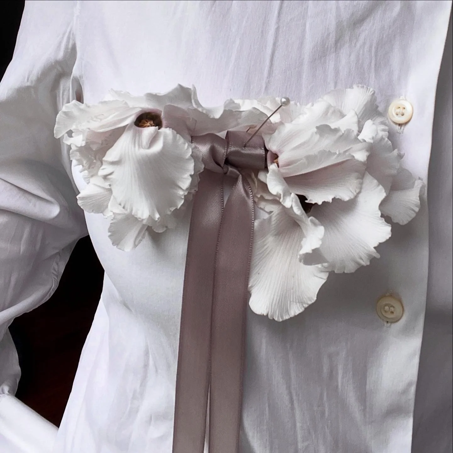 White shirt with large white flower and gray ribbon corsage, held together with a pearl-headed pin and a button on the shirt.