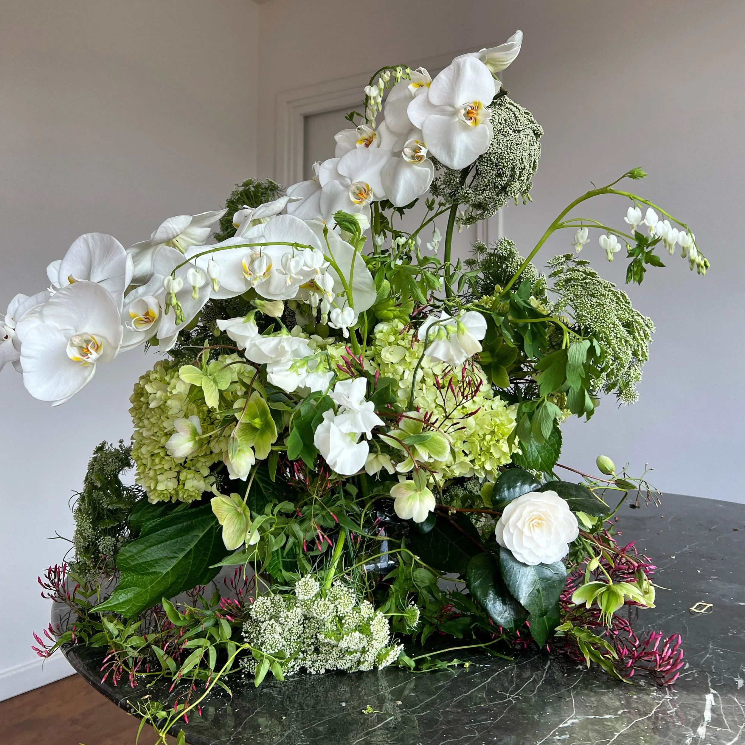 Arranged bouquet of white orchids, green hydrangeas, and other assorted flowers and greenery on a black marble table