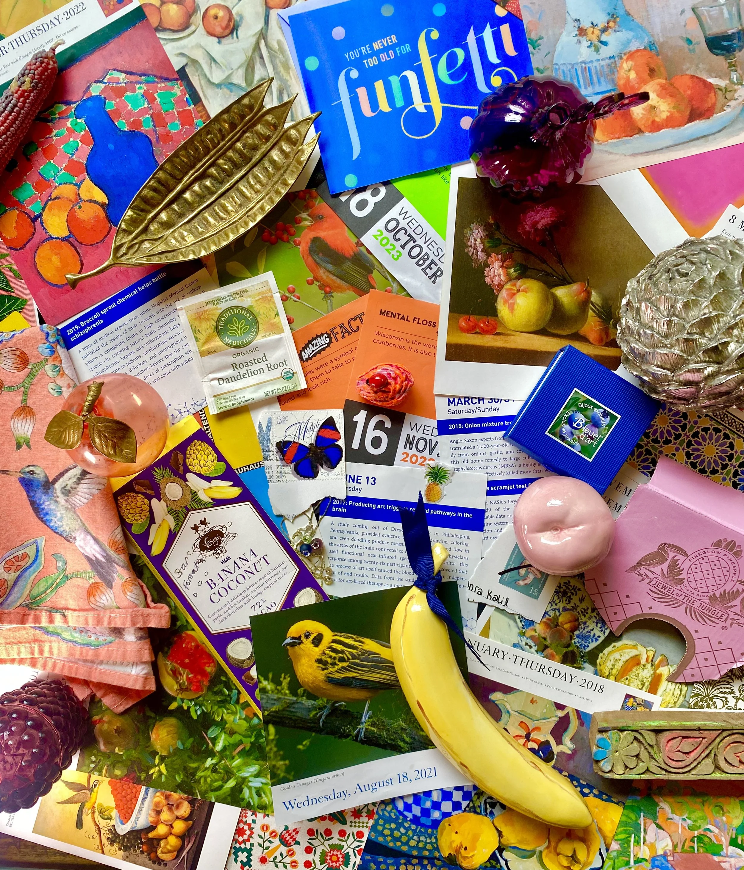 Seanra's inspiration: A colorful collage of various items including postcards, candies, flowers, a pineapple-shaped object, a butterfly sticker, a banana, a pink soap, a blueberry-themed card, and other decorative objects arranged on a surface.