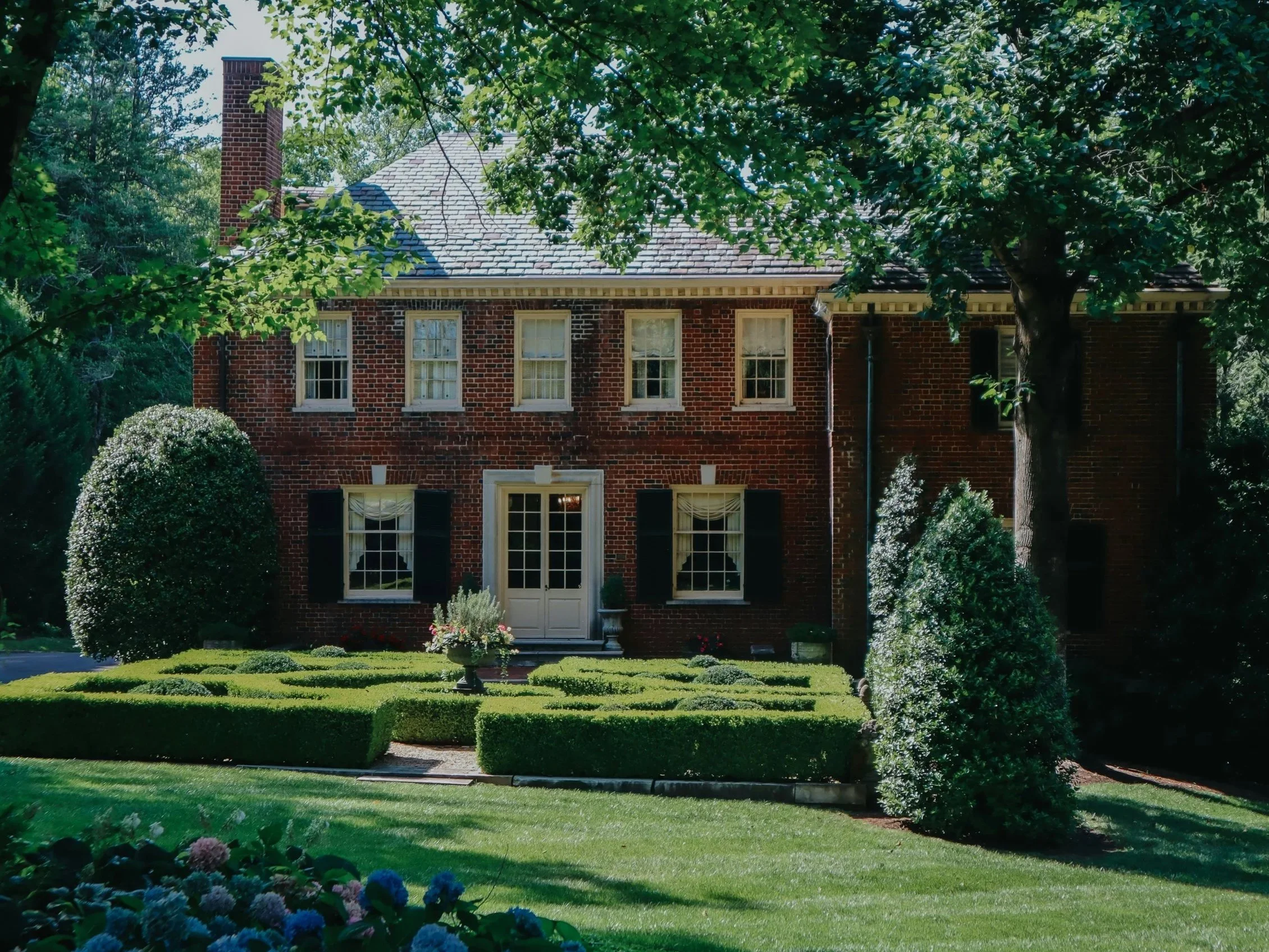 Large red brick luxury home with manicured garden, symbolizing discreet support services for high‑net‑worth families.