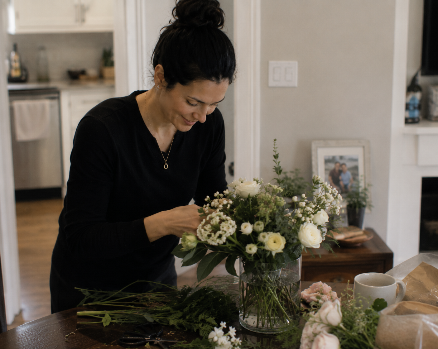 Woman arranging fresh flowers inside a calm, lived-in home environment, reflecting steady household presence and continuity-focused support.