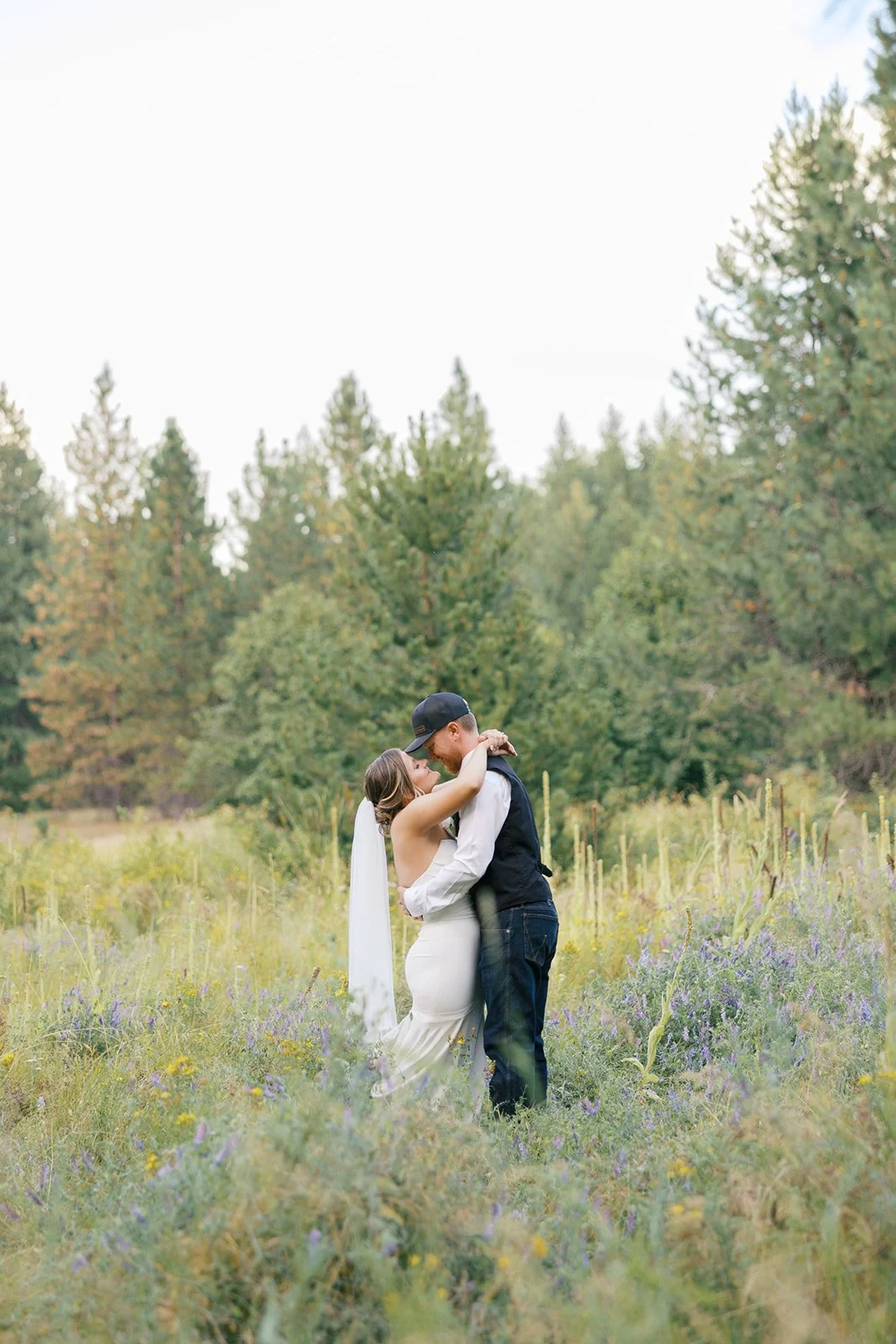 A couple embraces in a field of wildflowers with a forest in the background.
