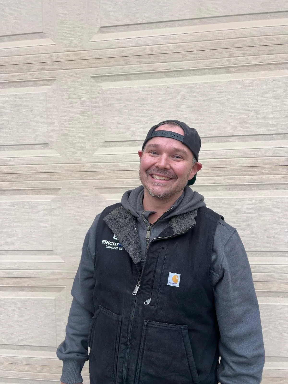 Close-up of a smiling woman with curly afro hair, wearing glasses, hoop earrings, layered necklaces, and a white striped shirt.
