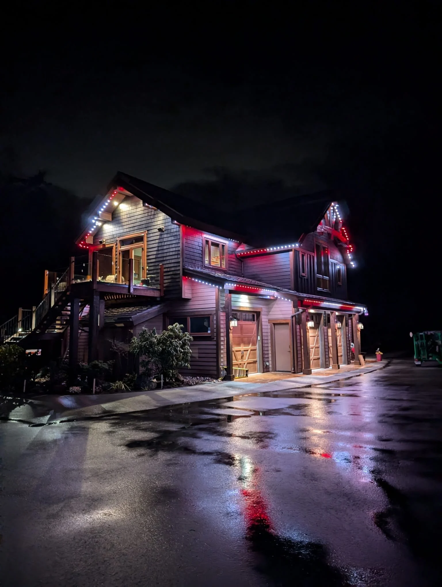 A house decorated with multicolored Christmas lights at night, with reflections on the wet pavement.
