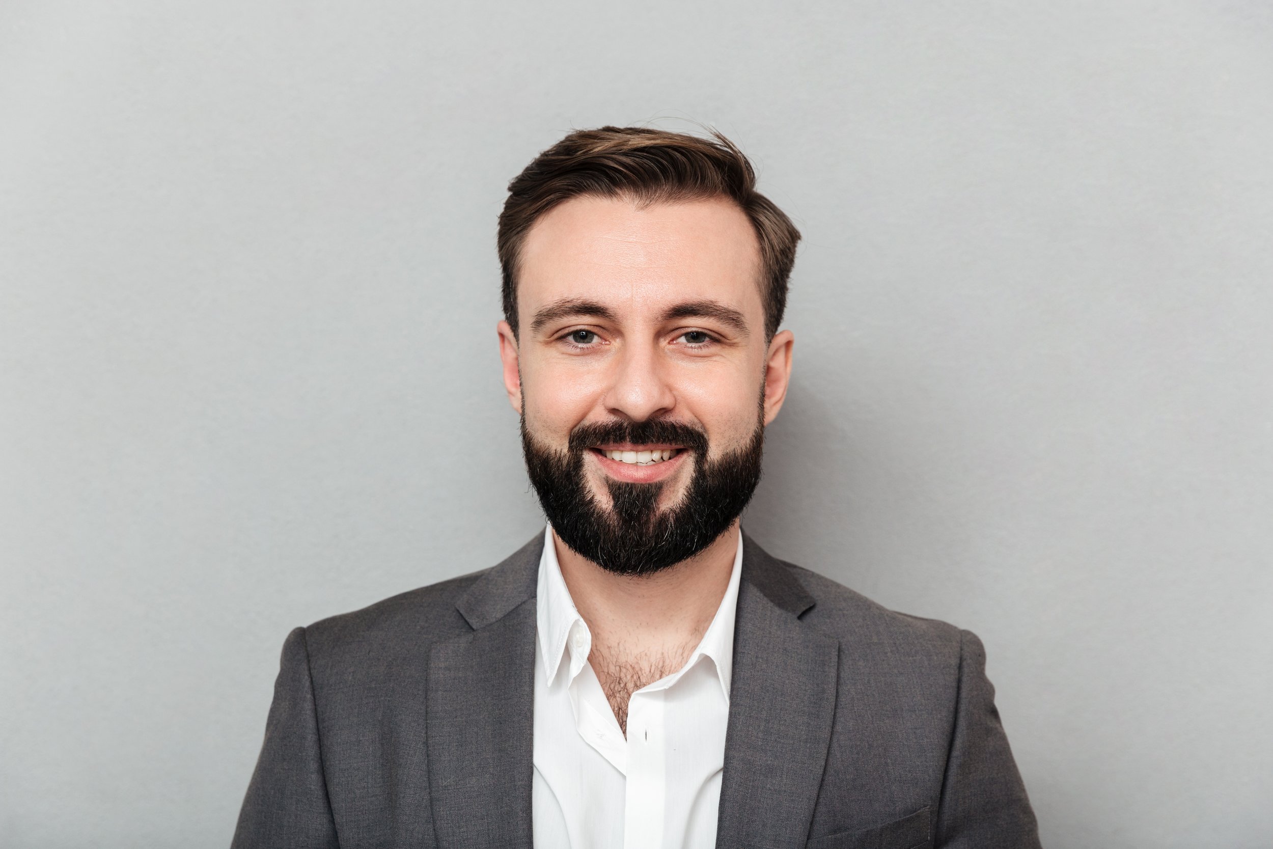 close-up-portrait-young-bearded-man-white-shirt-jacket-posing-camera-with-broad-smile-isolated-gray.jpg