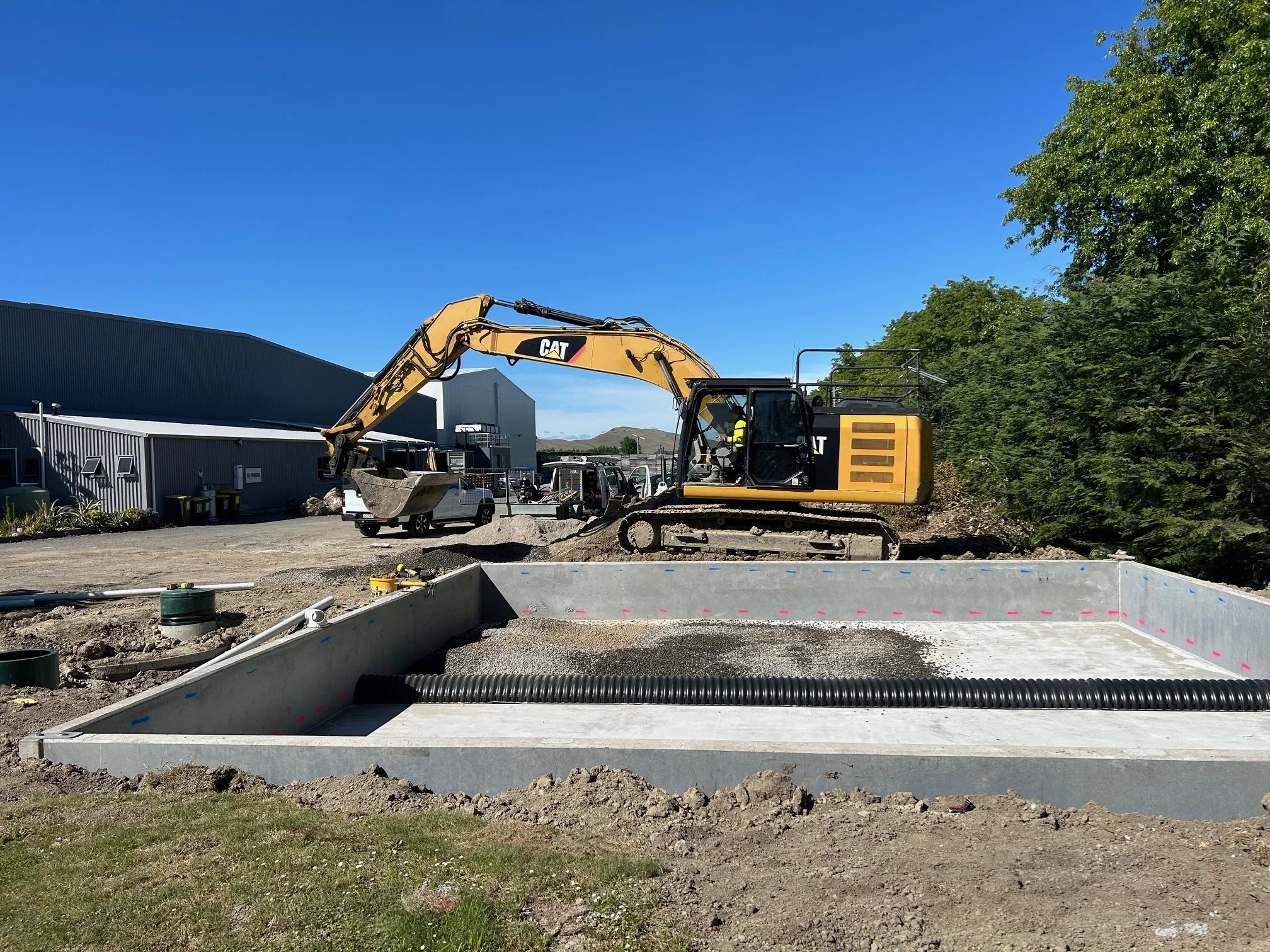Photo of a concrete filter being installed by a yellow digger on a sunny day on a commercial site.