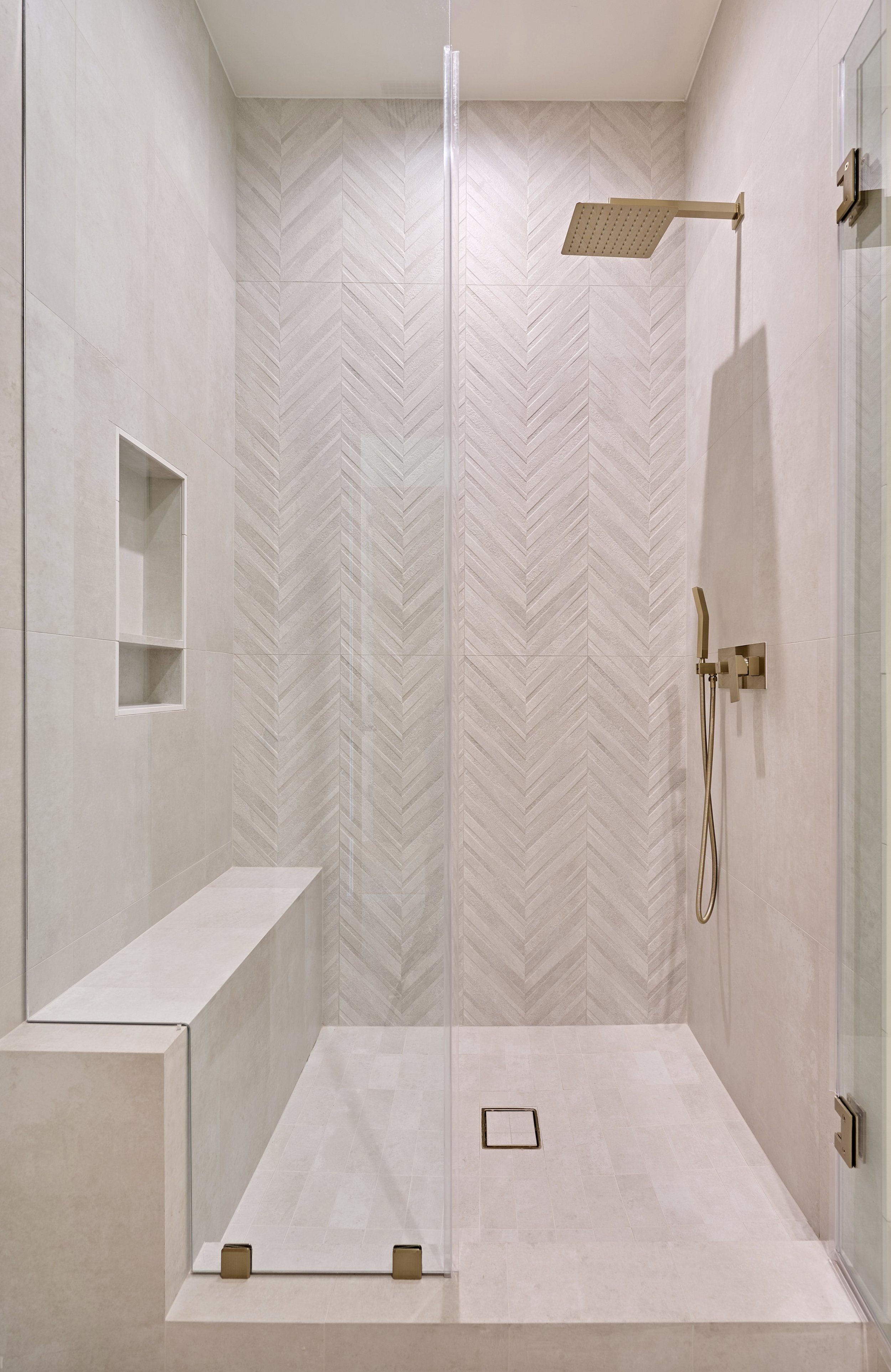 Modern minimalist shower with a glass door, rain showerhead, and built-in niche for toiletries, all in neutral tones.