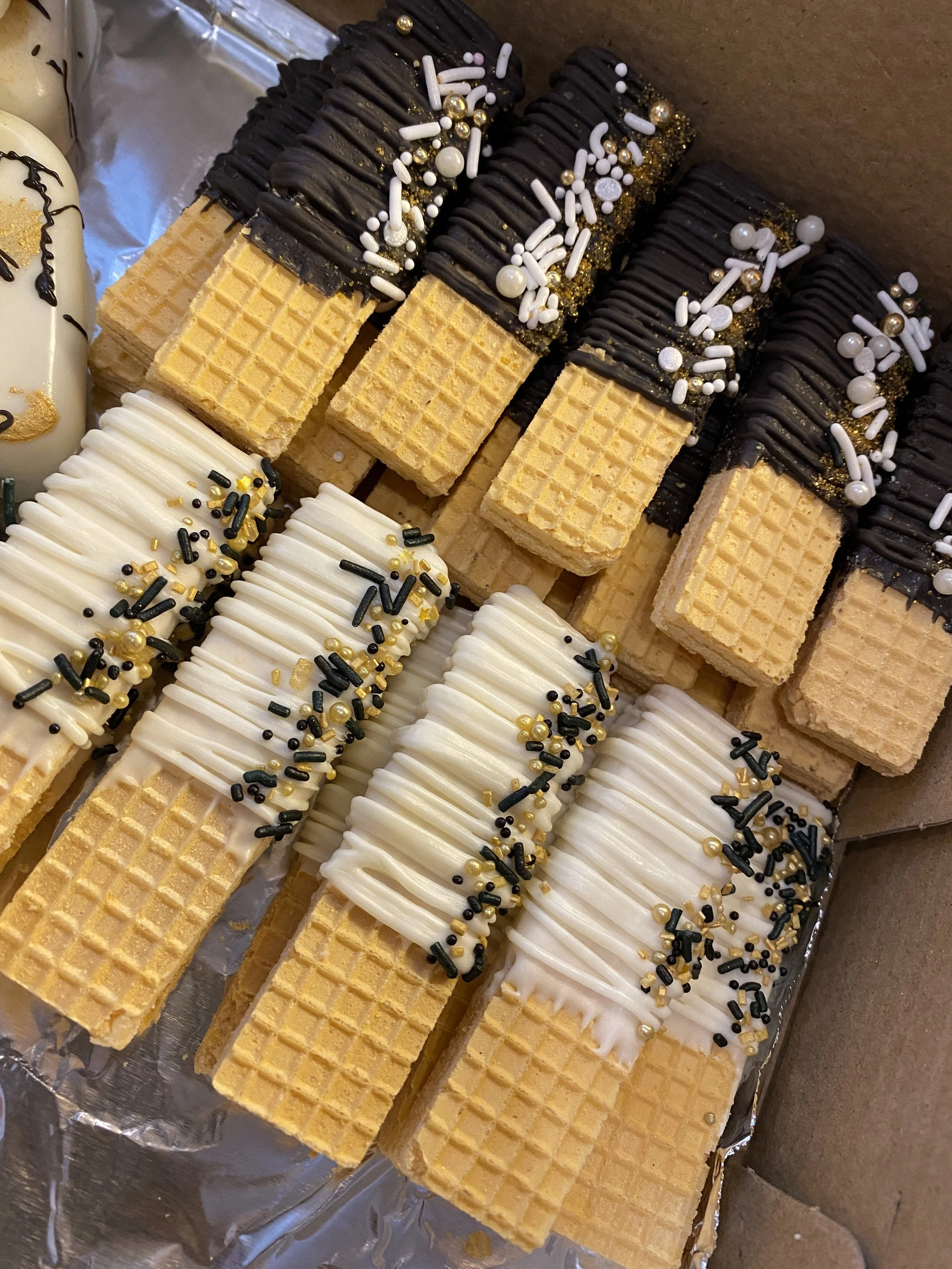 Close-up of assorted rectangular wafer cookies decorated with white and dark chocolate, sprinkles, and edible gold beads, arranged on a sheet of foil.
