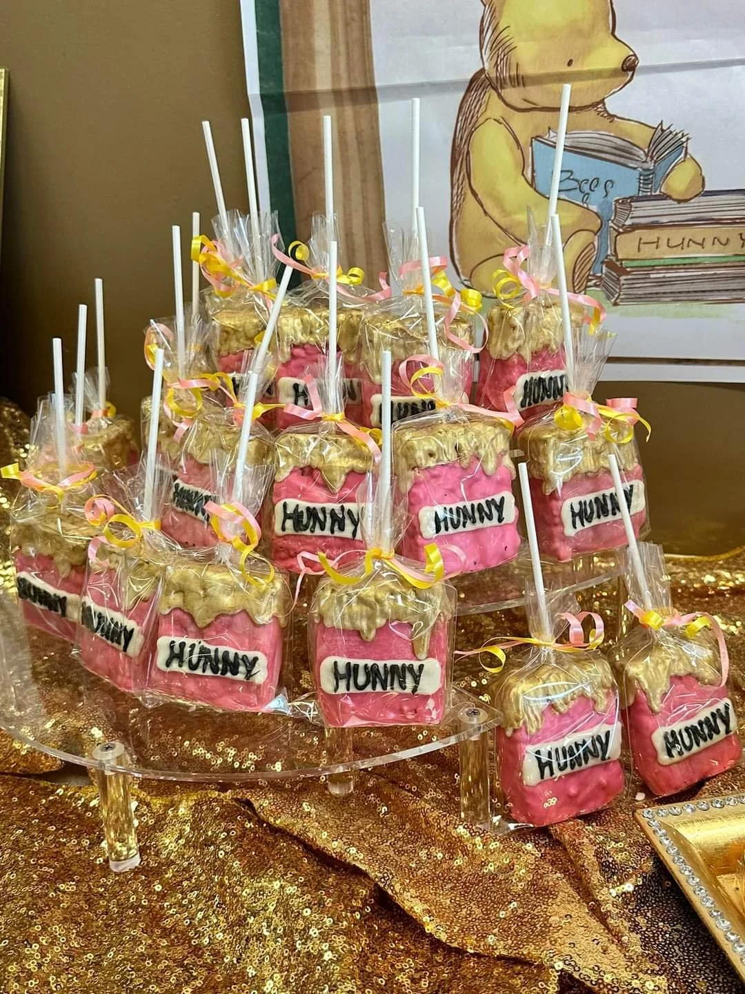 Pink and gold cookies decorated to look like honey jars, labeled "Hunny," displayed on a gold sequin tablecloth at a party.