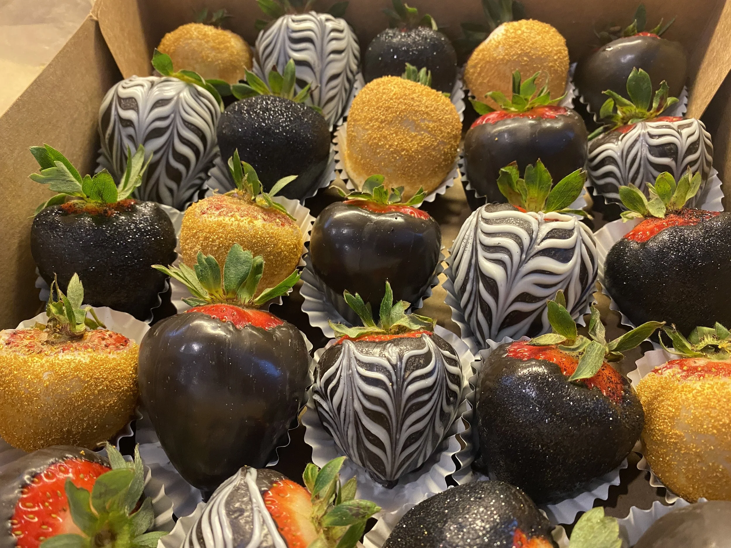 A collection of strawberries, some coated in dark chocolate, others dipped in white chocolate with zebra stripe decoration, and some covered in yellow sugar crystals.
