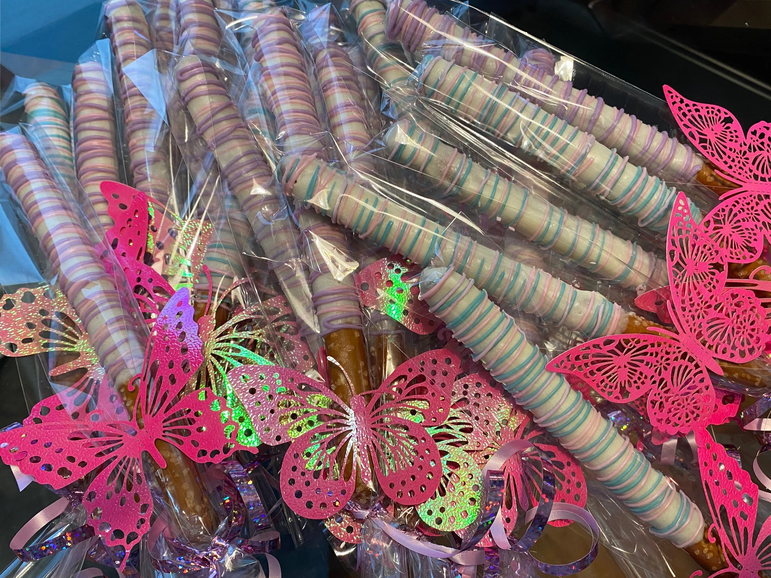 A collection of colorful unicorn horn-shaped lollipops wrapped in clear plastic, decorated with pink butterfly and butterfly-shaped stickers.