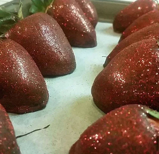 Close-up of fresh strawberries covered with red glitter, arranged on a white surface.