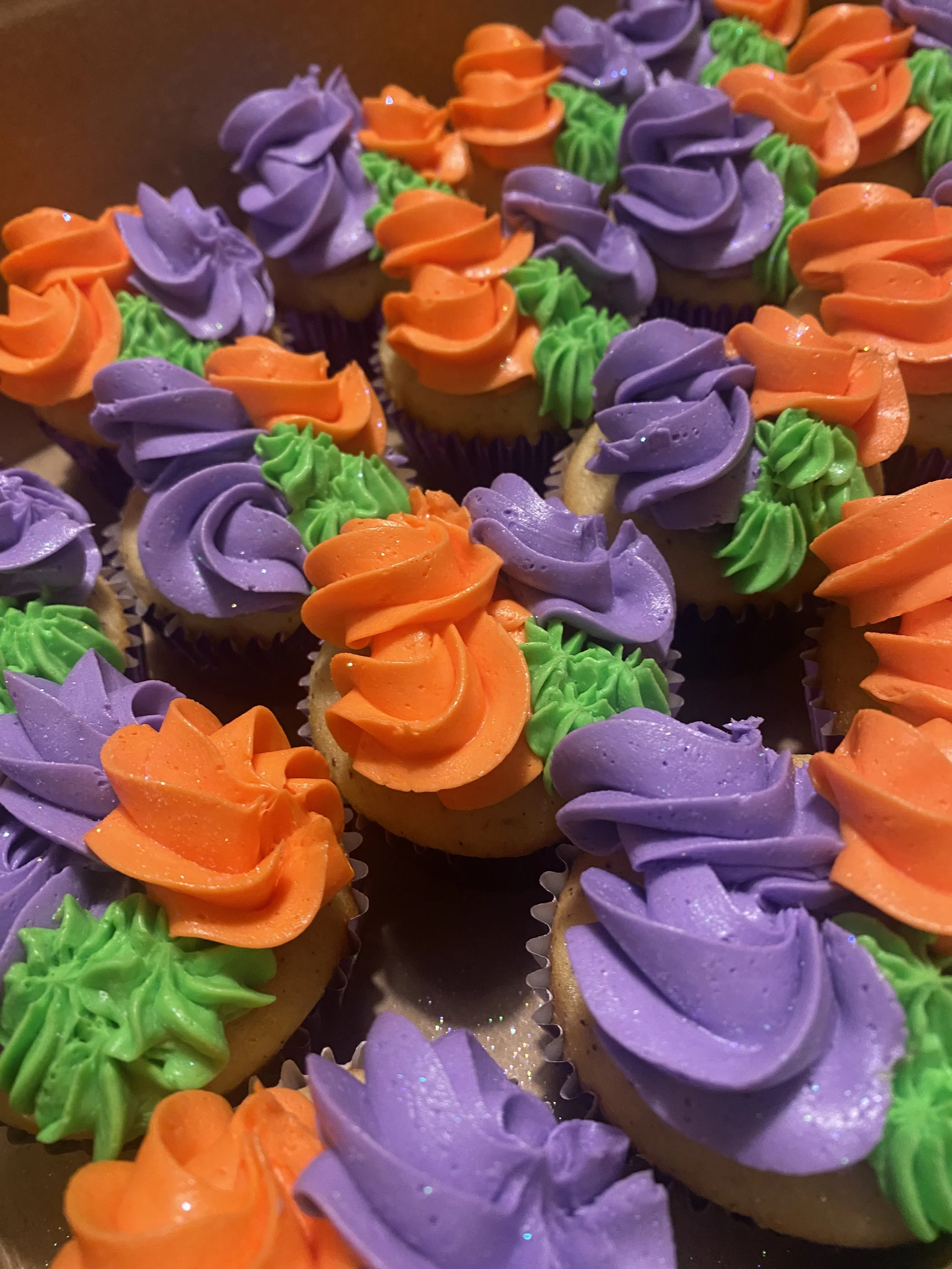 Close-up of Halloween-themed cupcakes decorated with purple, orange, and green frosting.