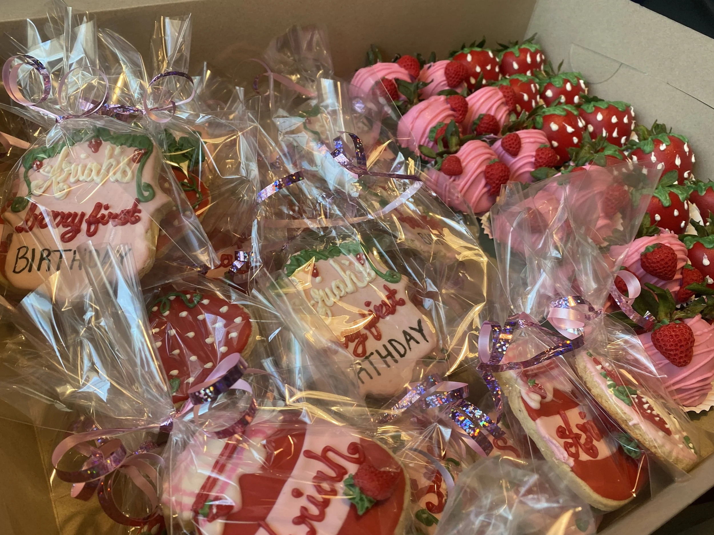Assorted strawberries and decorated cookies, some wrapped in clear plastic with pink ribbons, for a birthday celebration.