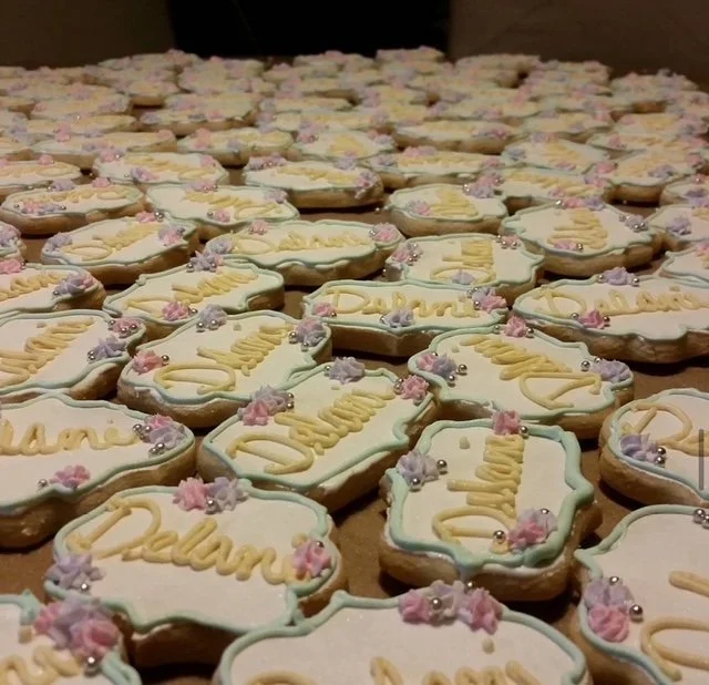Multiple decorated cookies with the words "Dulan" written on each, adorned with pink and purple flowers and small silver beads.
