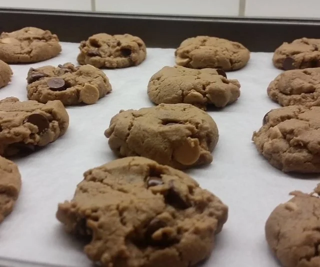 Freshly baked chocolate chip cookies on a baking sheet lined with parchment paper.