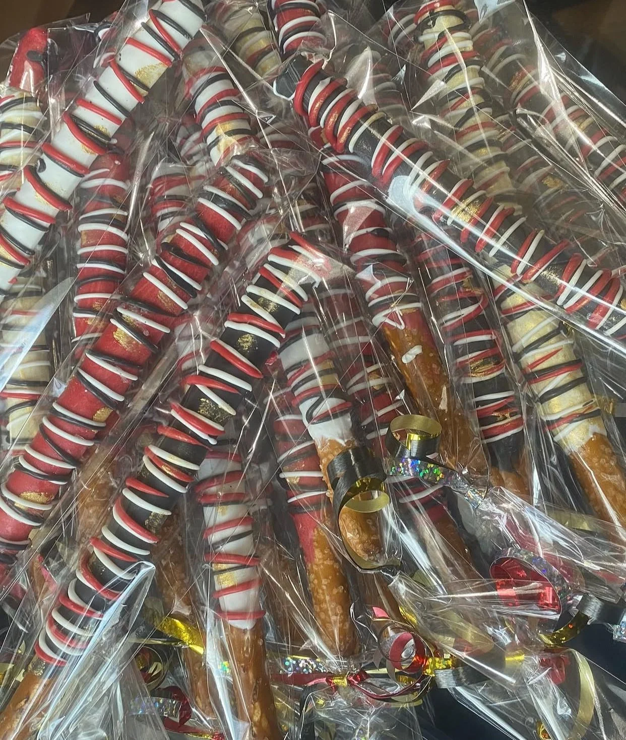 A pile of candy cane shaped lollipops wrapped in clear plastic with red, black, and white swirled ribbons.