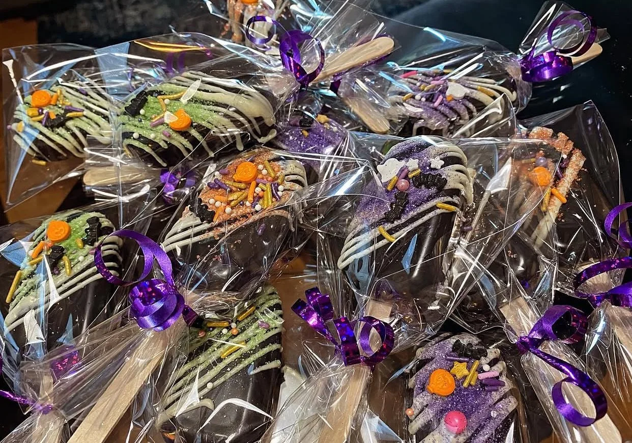Halloween-themed decorated cookies wrapped in clear plastic with purple ribbons.