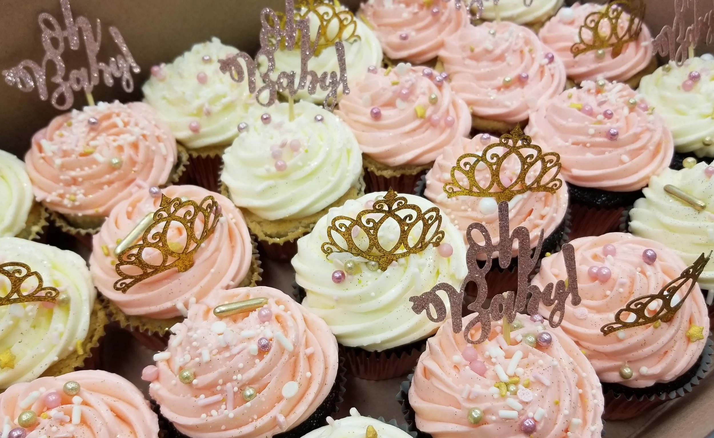 Assorted cupcakes with pink and white frosting topped with colorful sprinkles and decorative 'Happy Birthday' toppers.