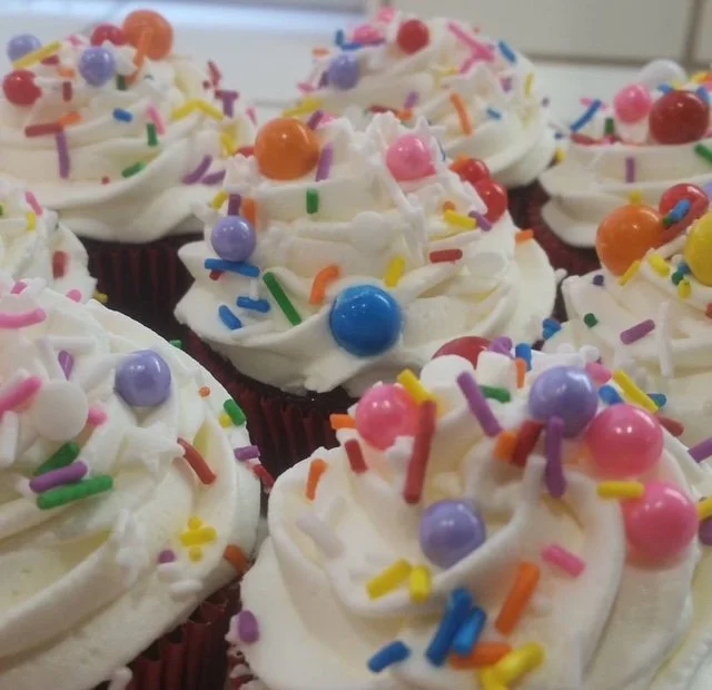 Cupcakes with white frosting, colorful sprinkles, and round candy toppings