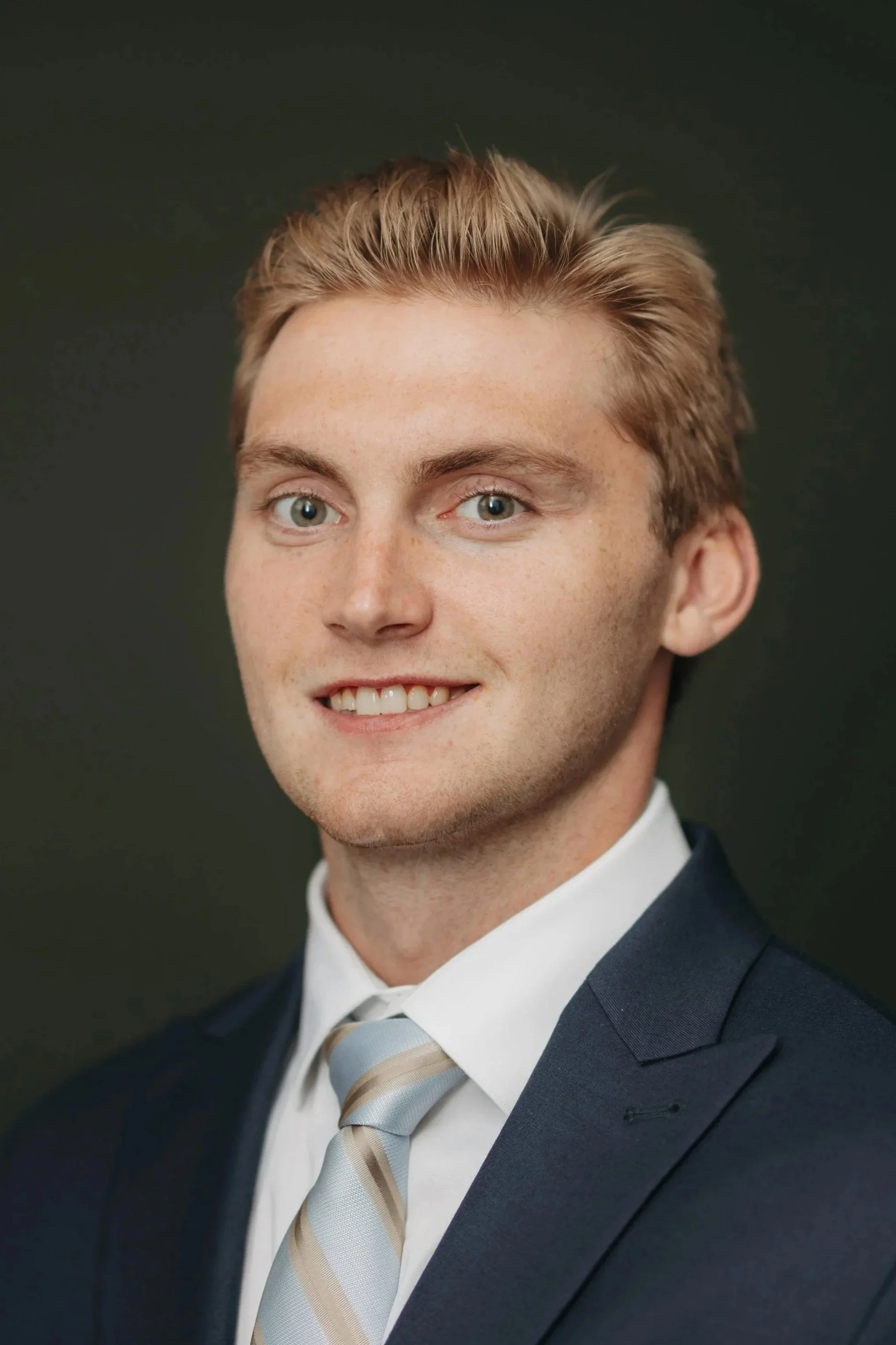 A young man with short brown hair, wearing an orange and black hockey jersey, smiling at the camera against a gray background.