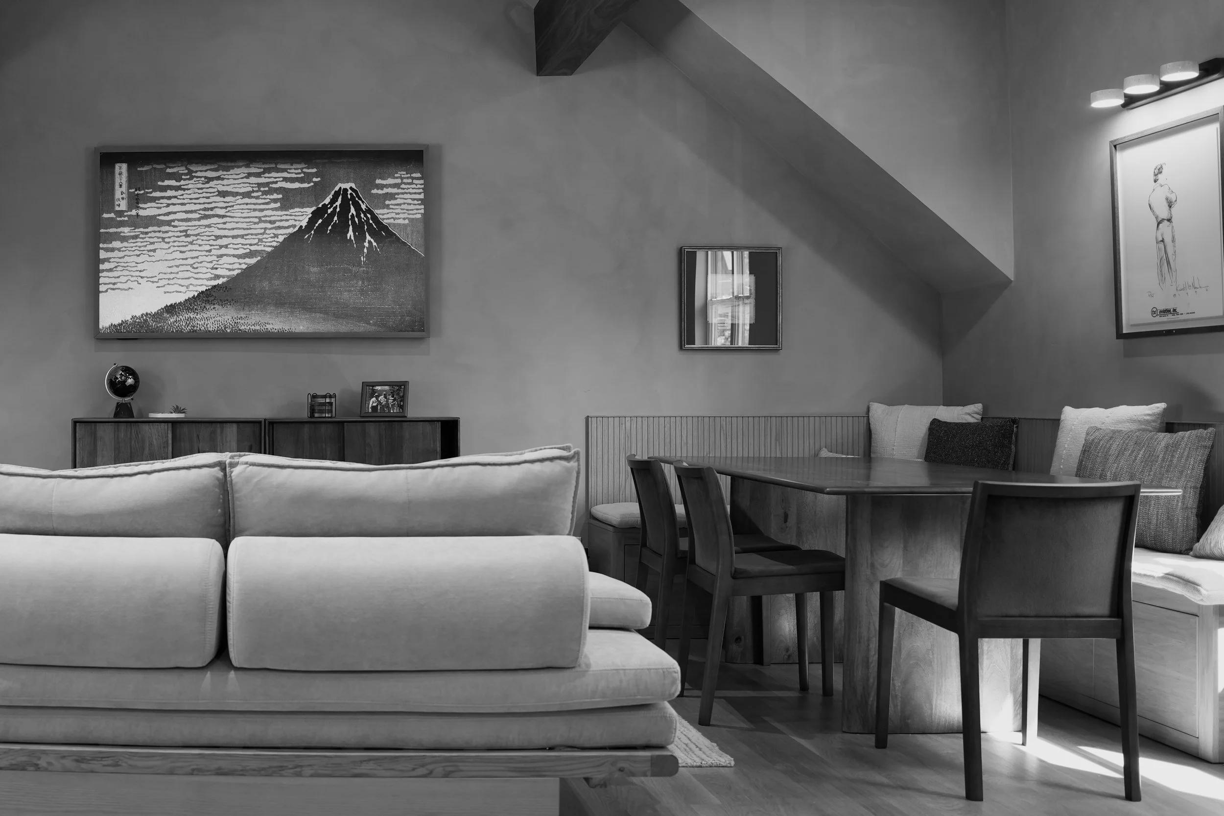 Living room with a sofa, a wooden dining table with chairs, framed artwork on the walls, and a sideboard with decorative items.