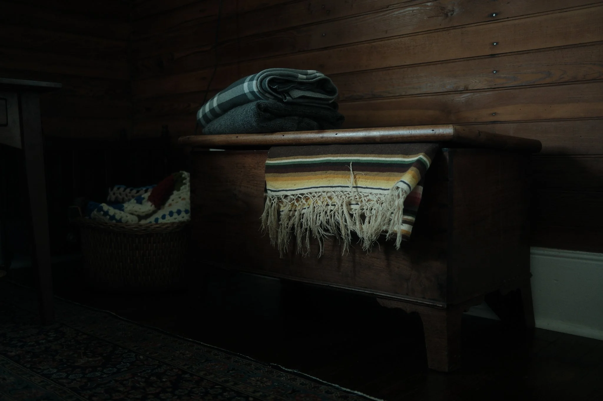 A wooden wall with a bunch of folded clothes or fabrics on a shelf, and a basket with knitted items in a cozy room.