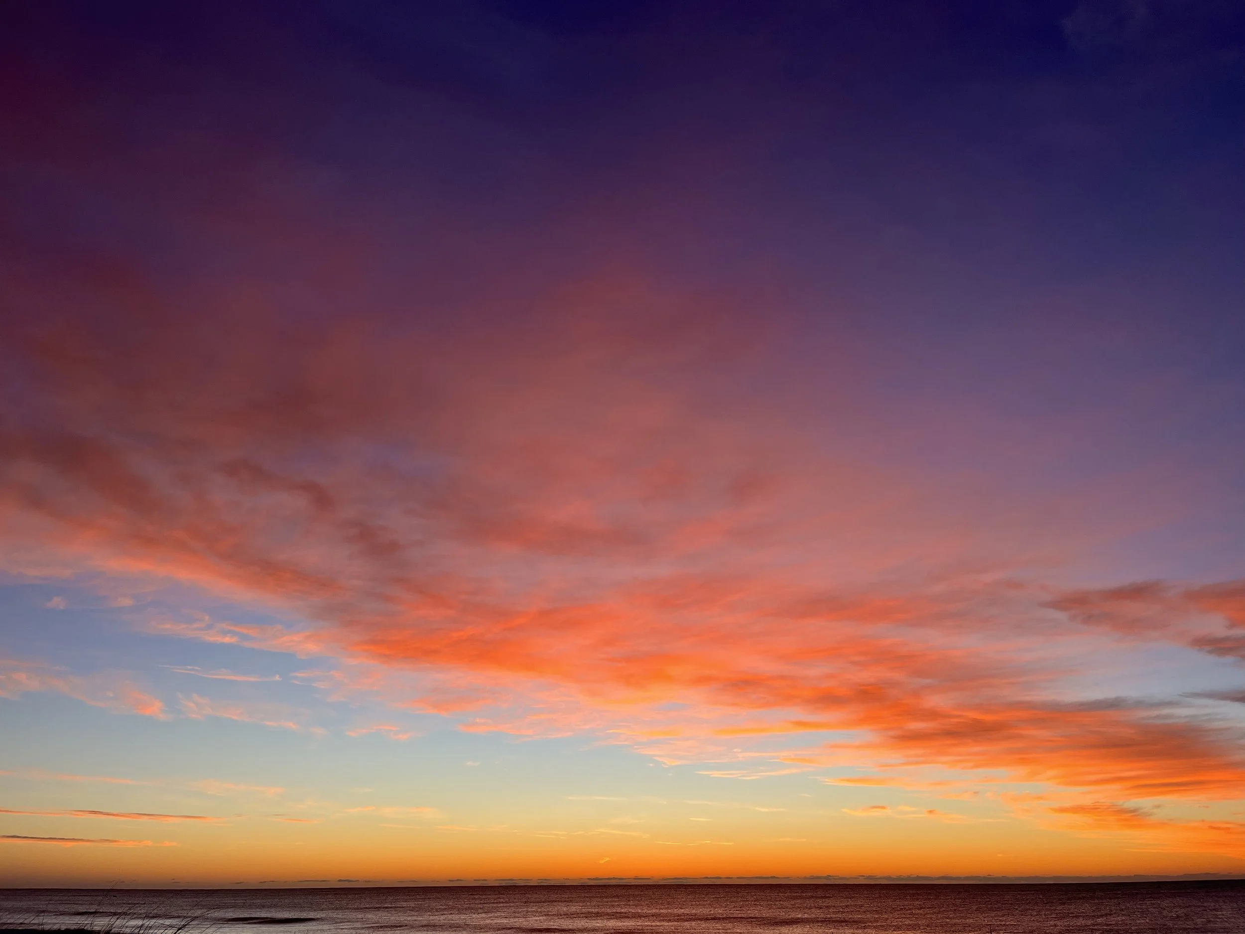 Colorful sunset over the ocean with orange, pink, purple, and blue clouds.