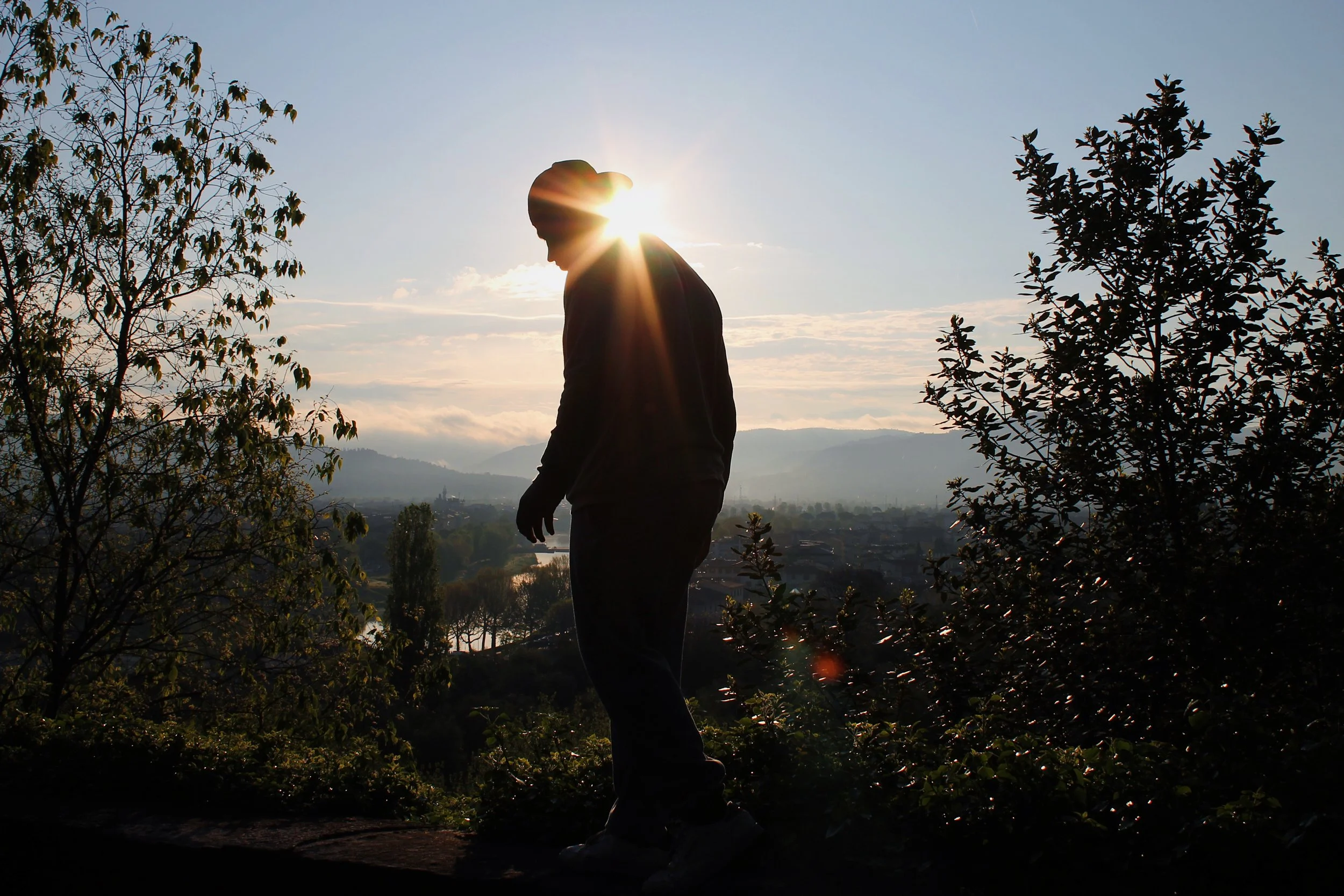 Silhouette of the company owner walking outdoors during sunrise in Florence, Italy, with trees and a cityscape in the background.