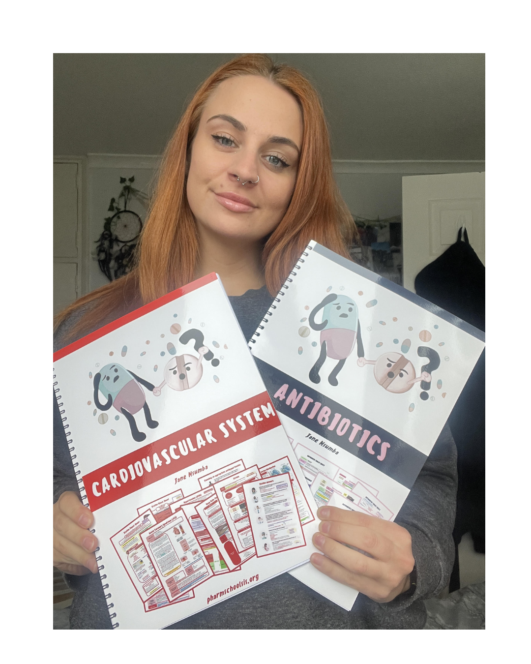 A young woman with red hair, light skin, and septum piercing holding educational materials about the human body, titled 'Cardiovascular System' and 'Antibiotics'.