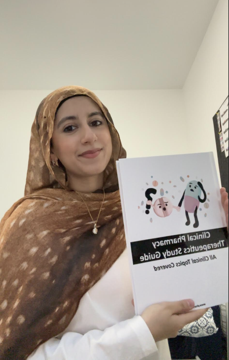 A woman wearing a brown scarf and white top holding a booklet titled "Clinical Pharmacy Therapeutics Study Guide" and an illustration of two cartoon characters holding hands.