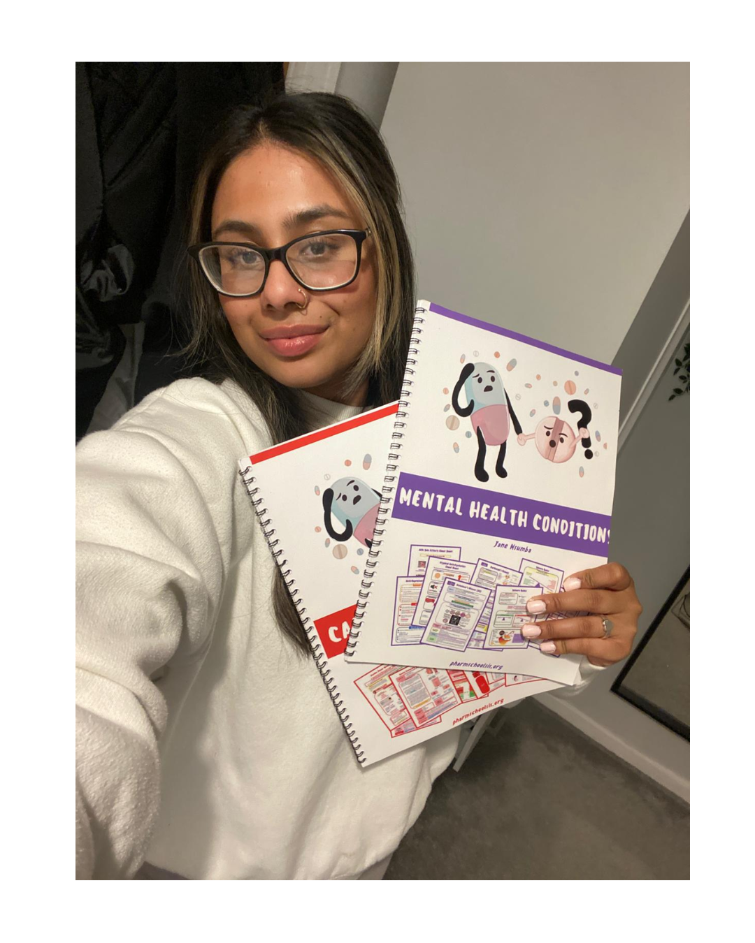 A woman with glasses holding two spiral-bound books about mental health conditions, one with a purple cover and cartoon illustrations, and the other with a red cover and similar illustrations.