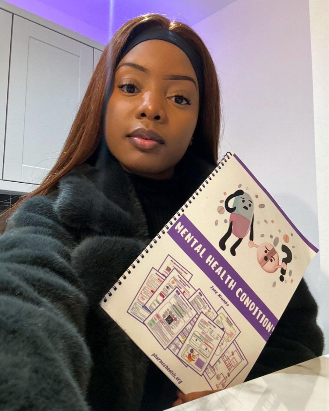 A woman taking a selfie while holding a pamphlet labeled 'Mental Health Conditions' with cartoon characters and informational content.