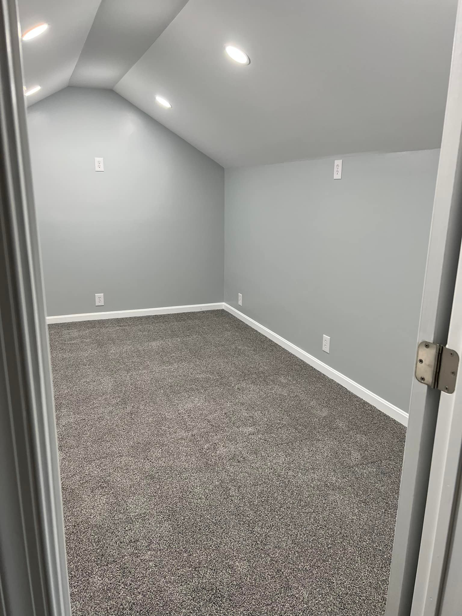 Empty room with gray walls, gray carpet, and recessed ceiling lights.