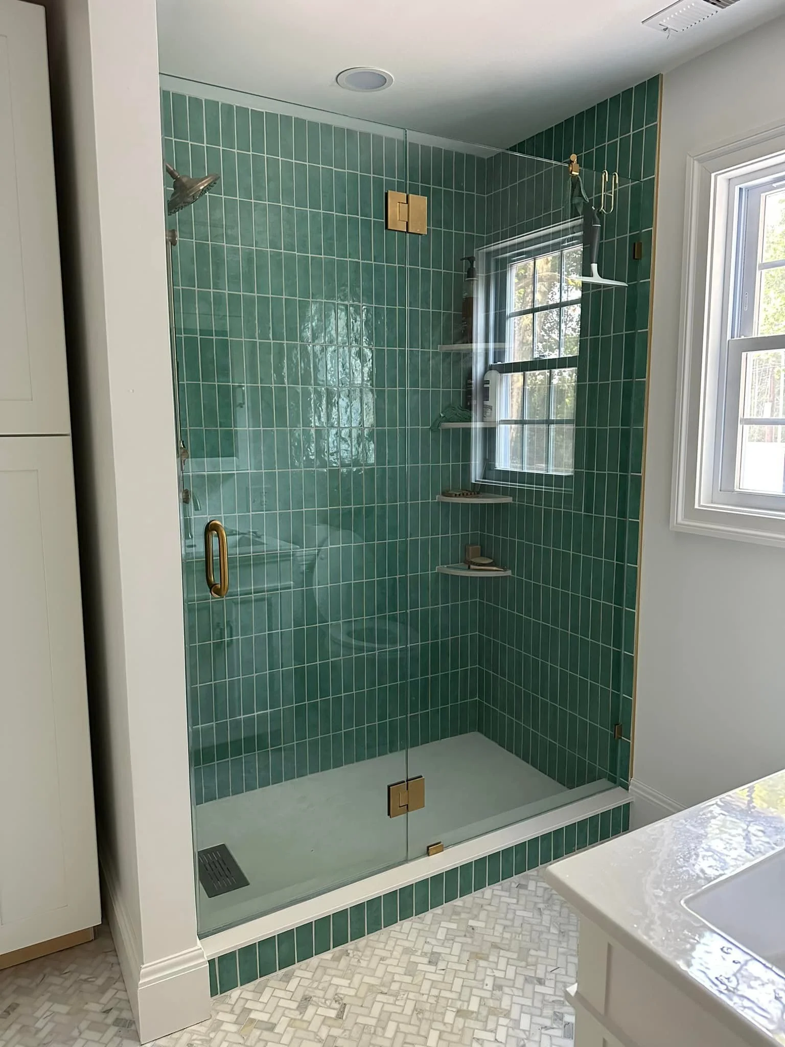 A modern shower with green tiles, a glass door, and a small window in a bathroom.