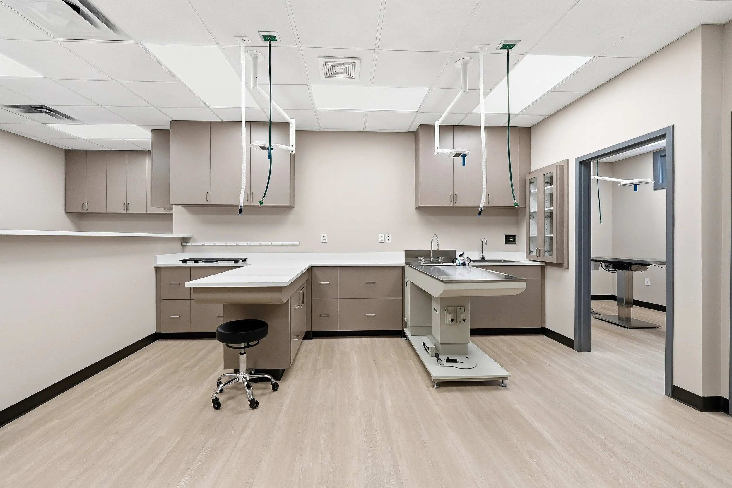 Open treatment area facing cabinets with two operating tables (one wet table, one dry), with medical equipment, sink, cabinets, and ceiling-mounted medical lights.
