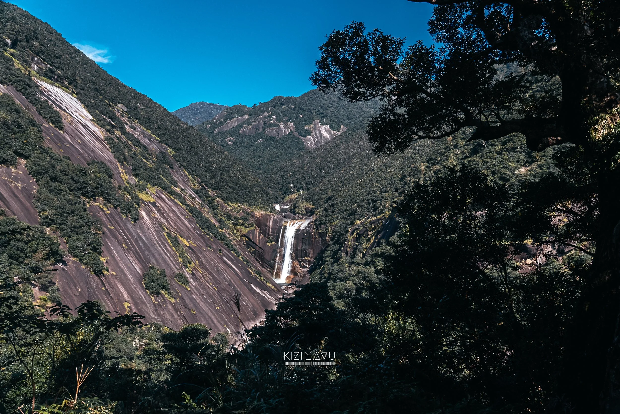 山と滝の自然の風景、青空と緑豊かな森林、樹木のシルエットが映る写真