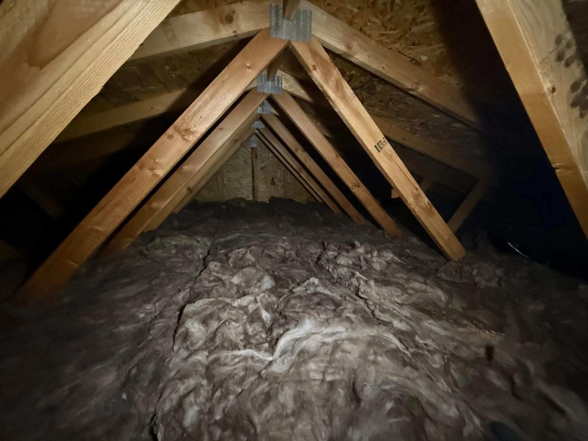 Attic space with exposed wooden beams and insulation on the floor.