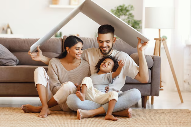 Family of three playing under a cardboard box fort in the living room