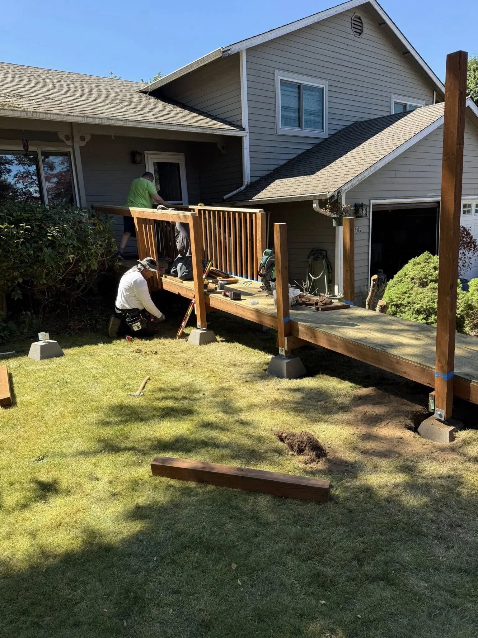 People installing a wooden deck in the backyard of a house on a sunny day.