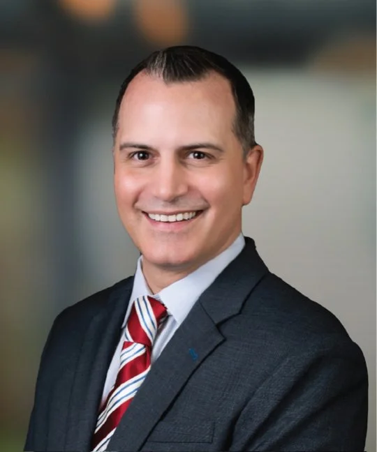 Smiling man in a suit with a striped tie, posing for a professional headshot.