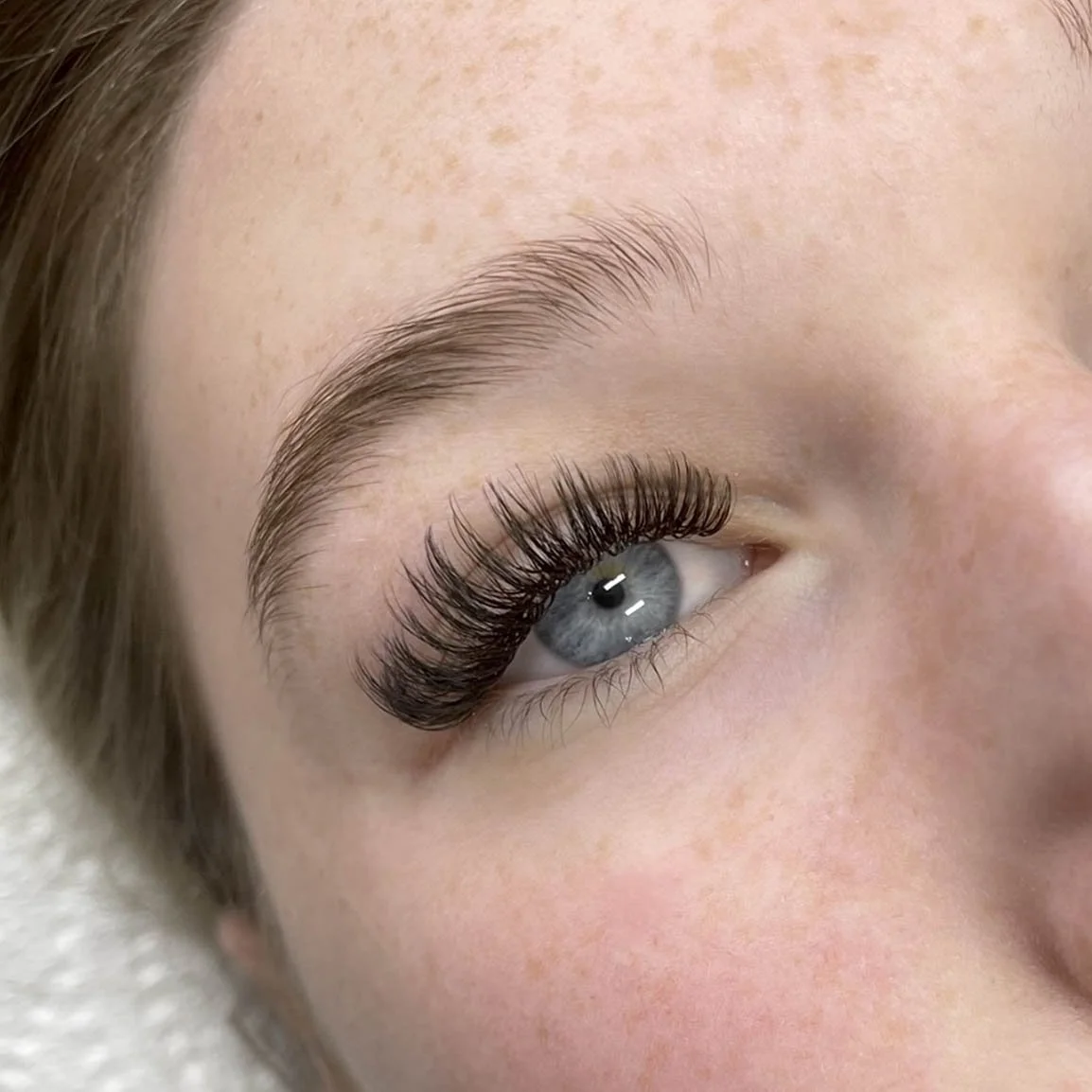 Close-up of a person's eye with long, curled eyelashes and well-groomed eyebrows.
