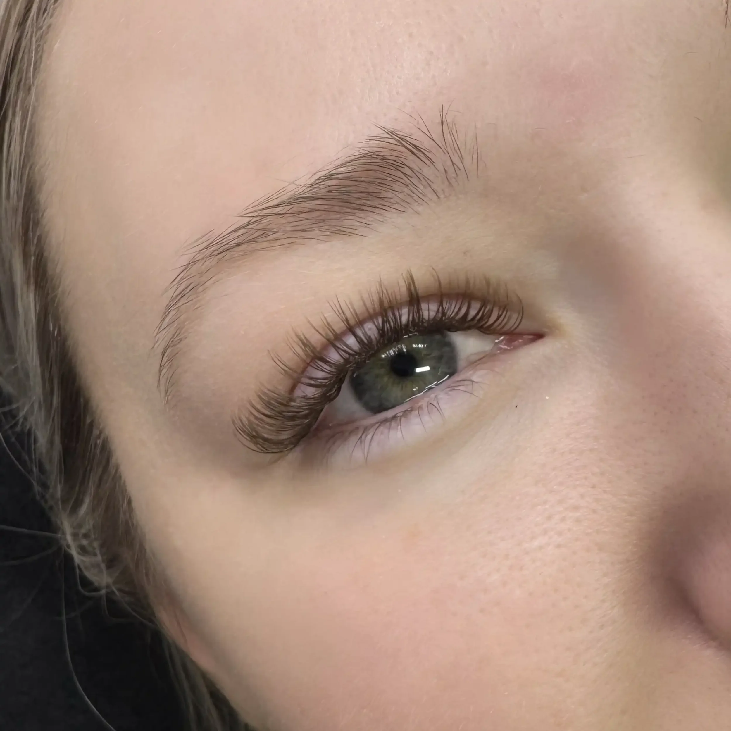 Close-up of a woman's eye with long curled eyelashes, green iris, and well-groomed eyebrow.