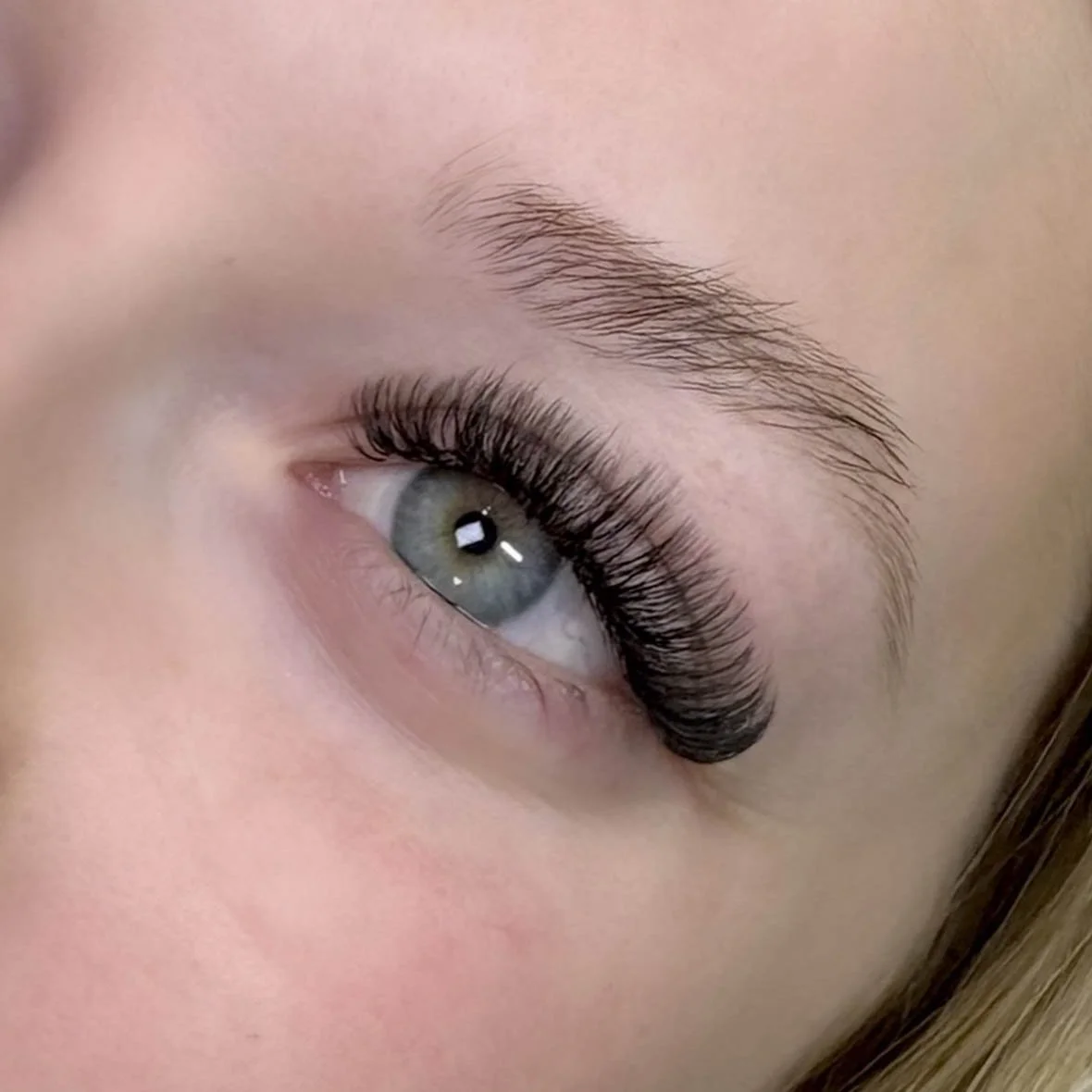 Close-up of a person's eye with long, curled eyelashes, light blue iris, and well-groomed eyebrow.